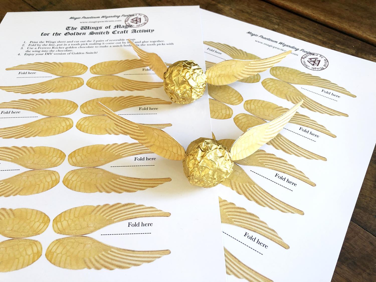 2 golden snitches made from Ferrero Rocher chocolate lying on pages of printable golden wings for snitches